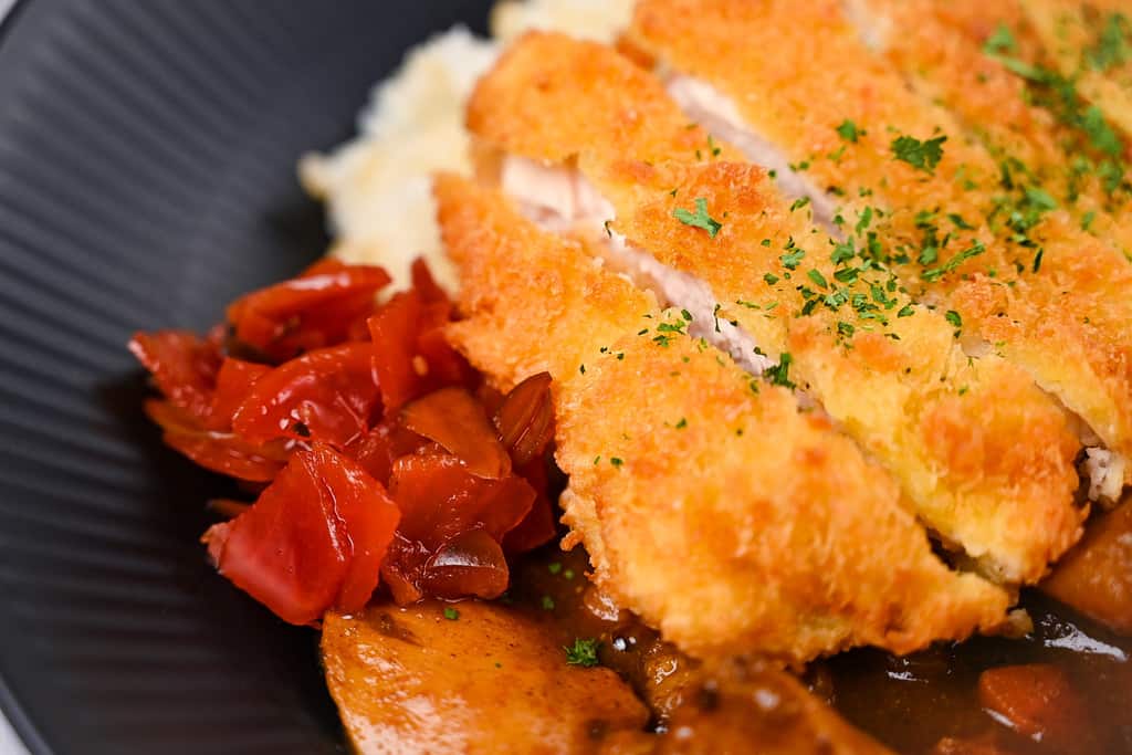 Chicken katsu curry with rice and pickles on a black plate close up
