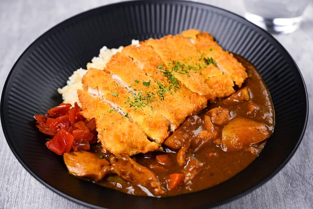 Chicken katsu curry with rice and pickles on a black plate side view