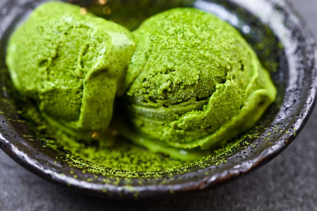two scoops of matcha green tea ice cream served in a black bowl side view