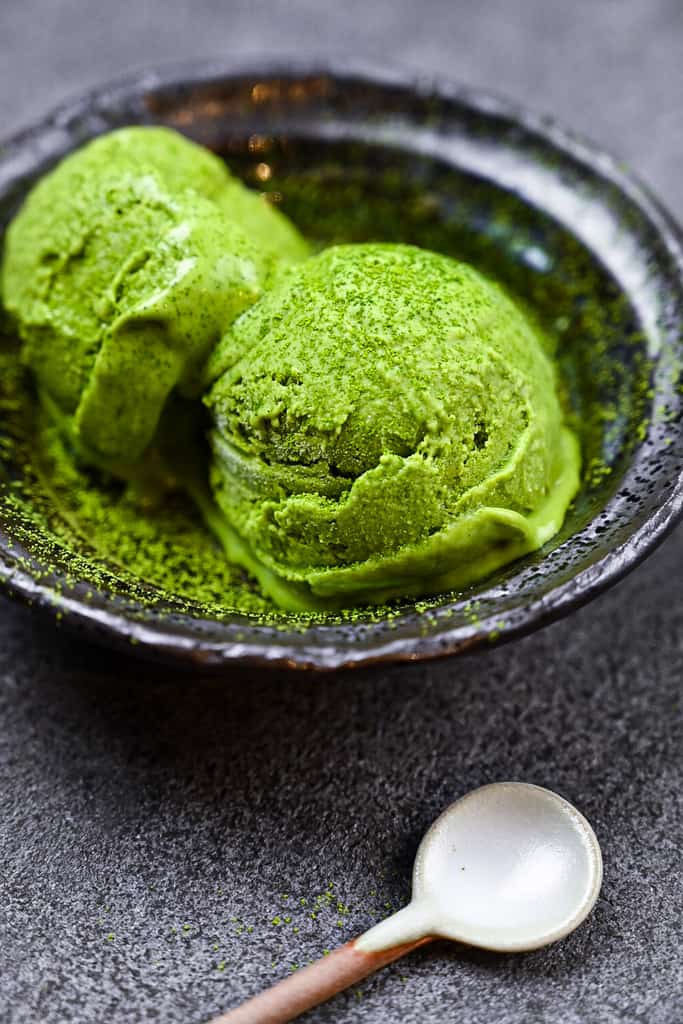 two scoops of matcha green tea ice cream served in a black bowl side view