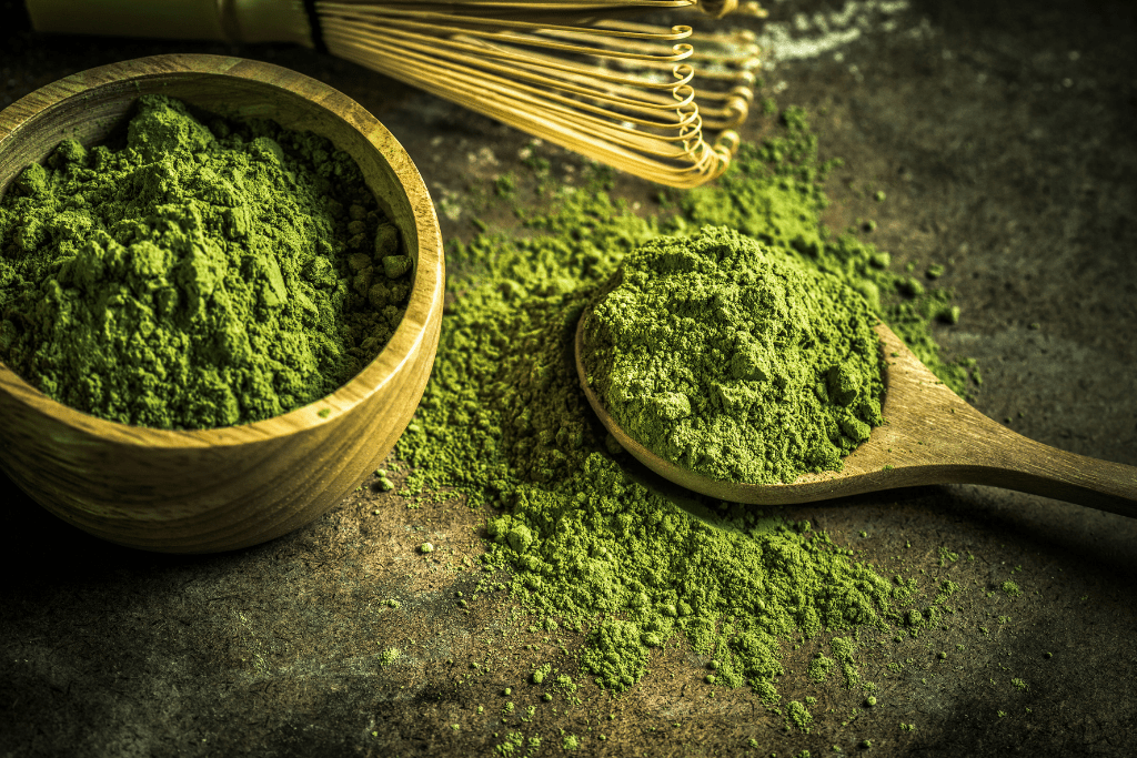 matcha tea powder on a spoon with bowl and whisk