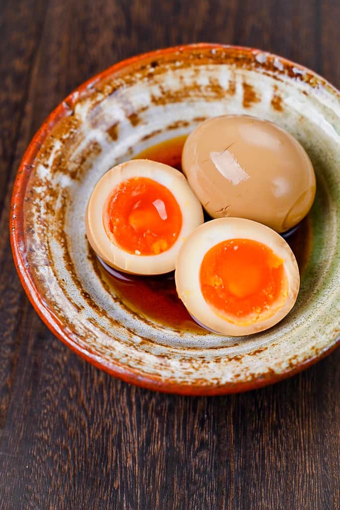 2 marinated ramen eggs arranged on a rust colored dish on a wooden surface