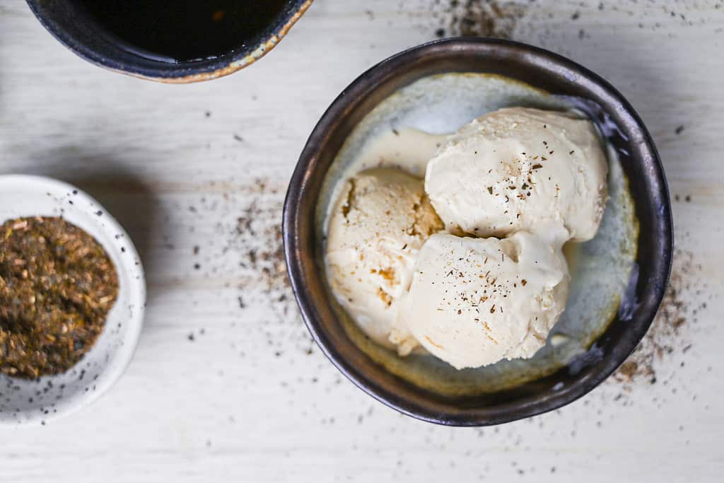 three scoops of hojicha ice cream in a brown bowl with loose tea and a cup of tea