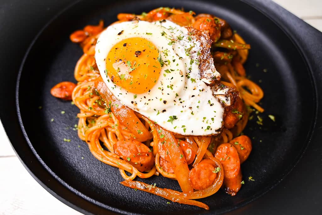 Spaghetti Napolitan (ketchup pasta) on a black plate topped with a fried egg close up