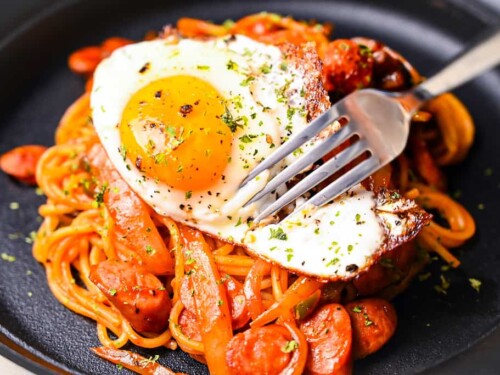 Fork cutting into fried egg on Spaghetti Napolitan (ketchup pasta)