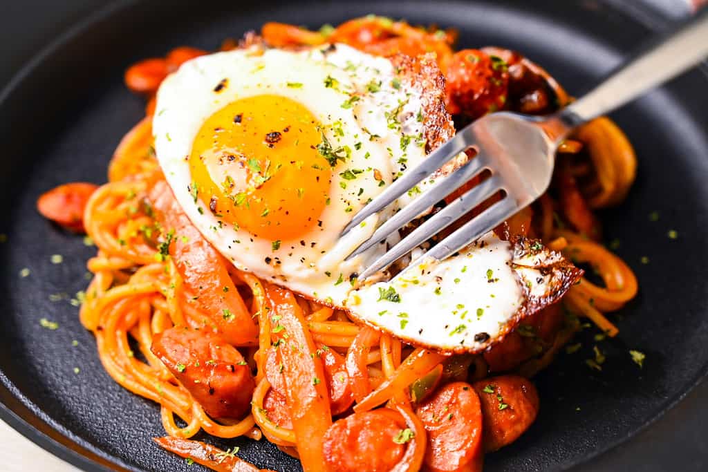 Fork cutting into fried egg on Spaghetti Napolitan (ketchup pasta)