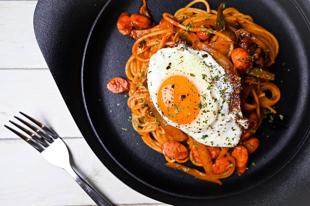 Spaghetti Napolitan (ketchup pasta) on a black plate topped with a fried egg top down