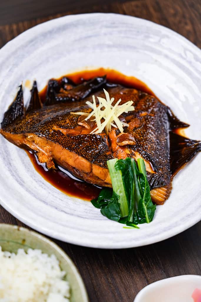 Sakana no nitsuke Japanese simmered fish on a white plate with ginger and bok choi