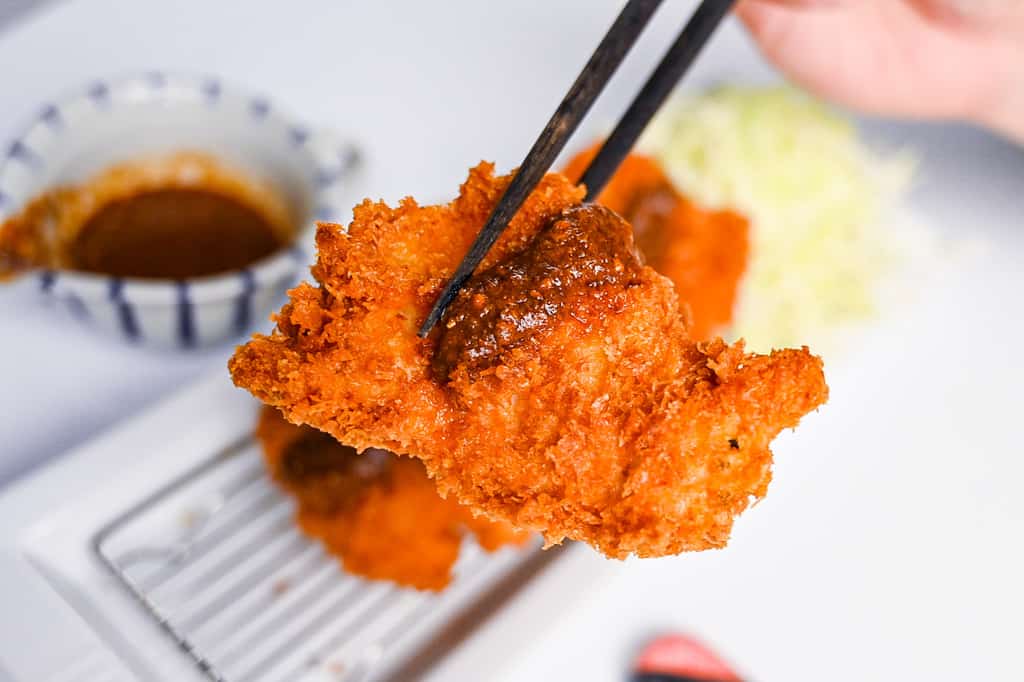 Japanese chicken katsu with homemade sauce held with black chopsticks