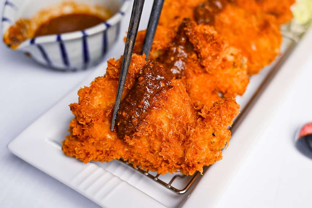 Japanese chicken katsu with homemade sauce held with black chopsticks