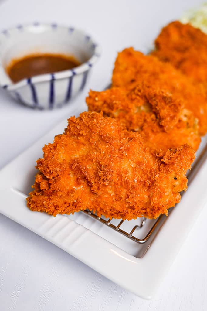 Japanese crispy chicken katsu served on a white rectangular plate with shredded cabbage and a jug of homemade katsu sauce