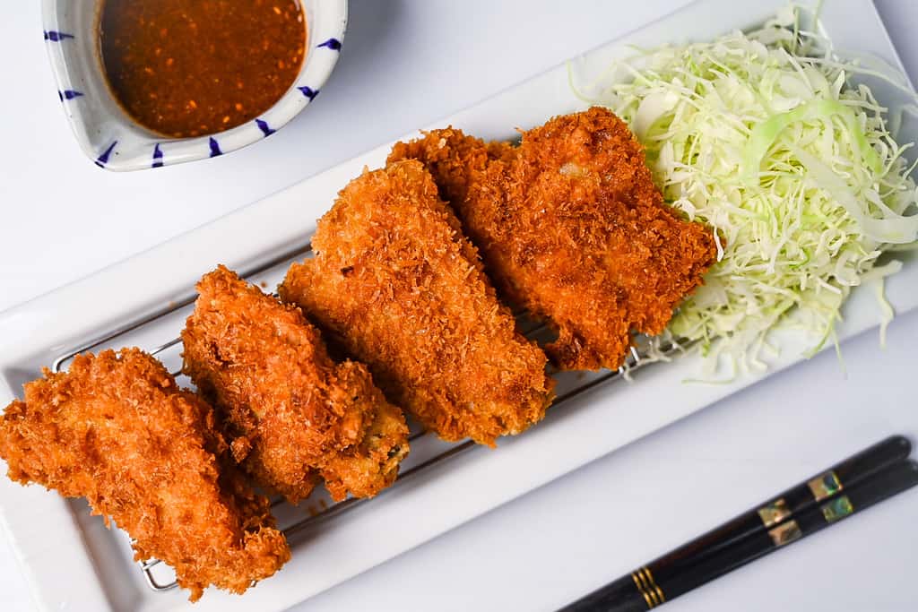 Japanese crispy chicken katsu served on a white rectangular plate with shredded cabbage and a jug of homemade katsu sauce top down