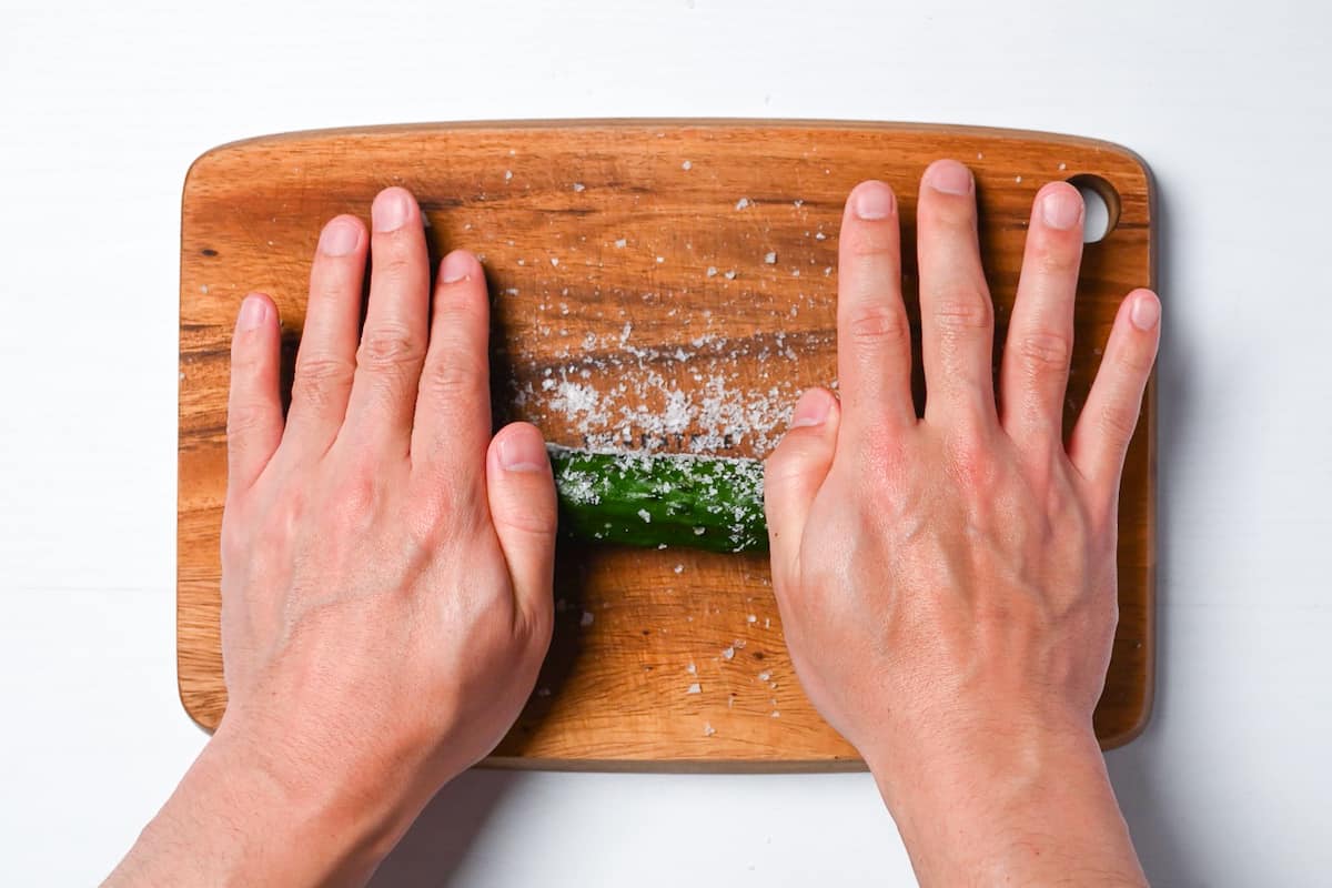 Rolling cucumber in salt on wooden chopping board