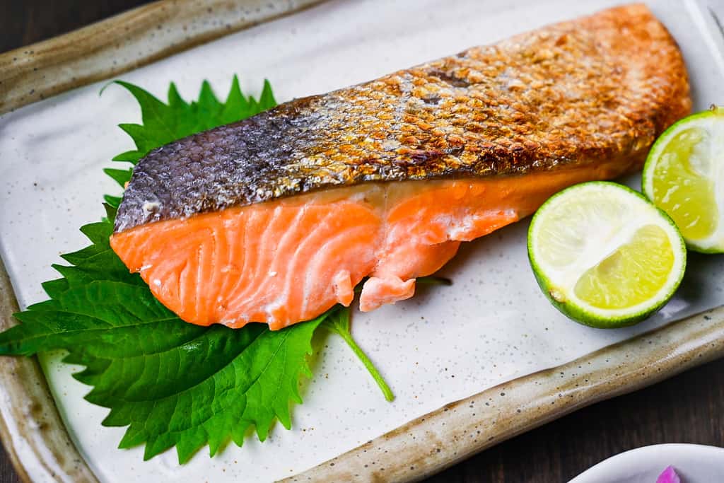 Shizake Japanese Salted Salmon served on a pale rectangular plate with sudachi and shiso leaves right side