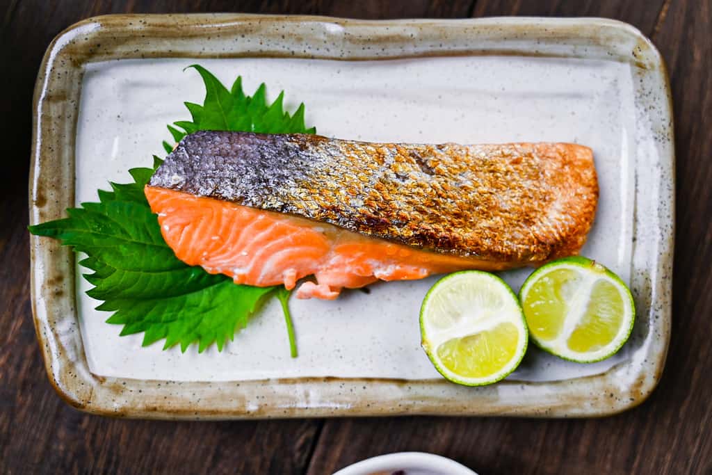 Shizake Japanese Salted Salmon served on a pale rectangular plate with sudachi and shiso leaves top down