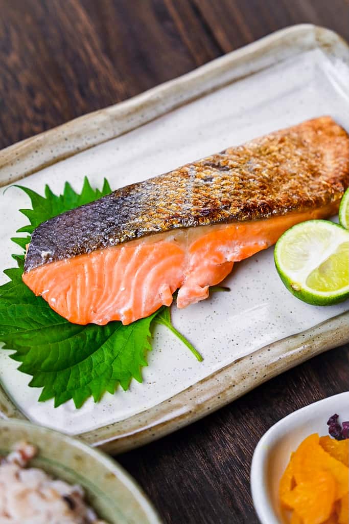 Shizake Japanese Salted Salmon served on a pale rectangular plate with sudachi and shiso leaves left side portrait