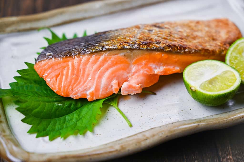 Shizake Japanese Salted Salmon served on a pale rectangular plate with sudachi and shiso leaves closeup