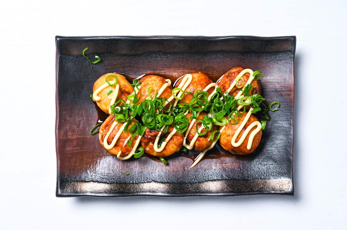 takoyaki on a plate topped with takoyaki sauce, Japanese mayonnaise and chopped spring onion