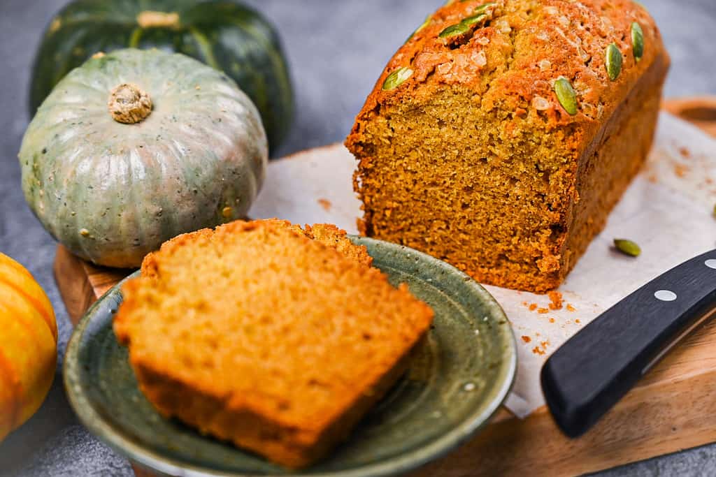 Kabocha pumpkin bread on a wooden chopping board with 2 slices