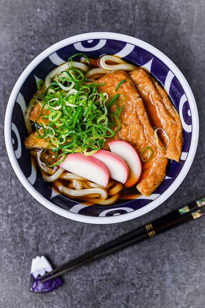 kitsune udon served in a blue and white bowl topped with spring onion and kamaboko fish cakes