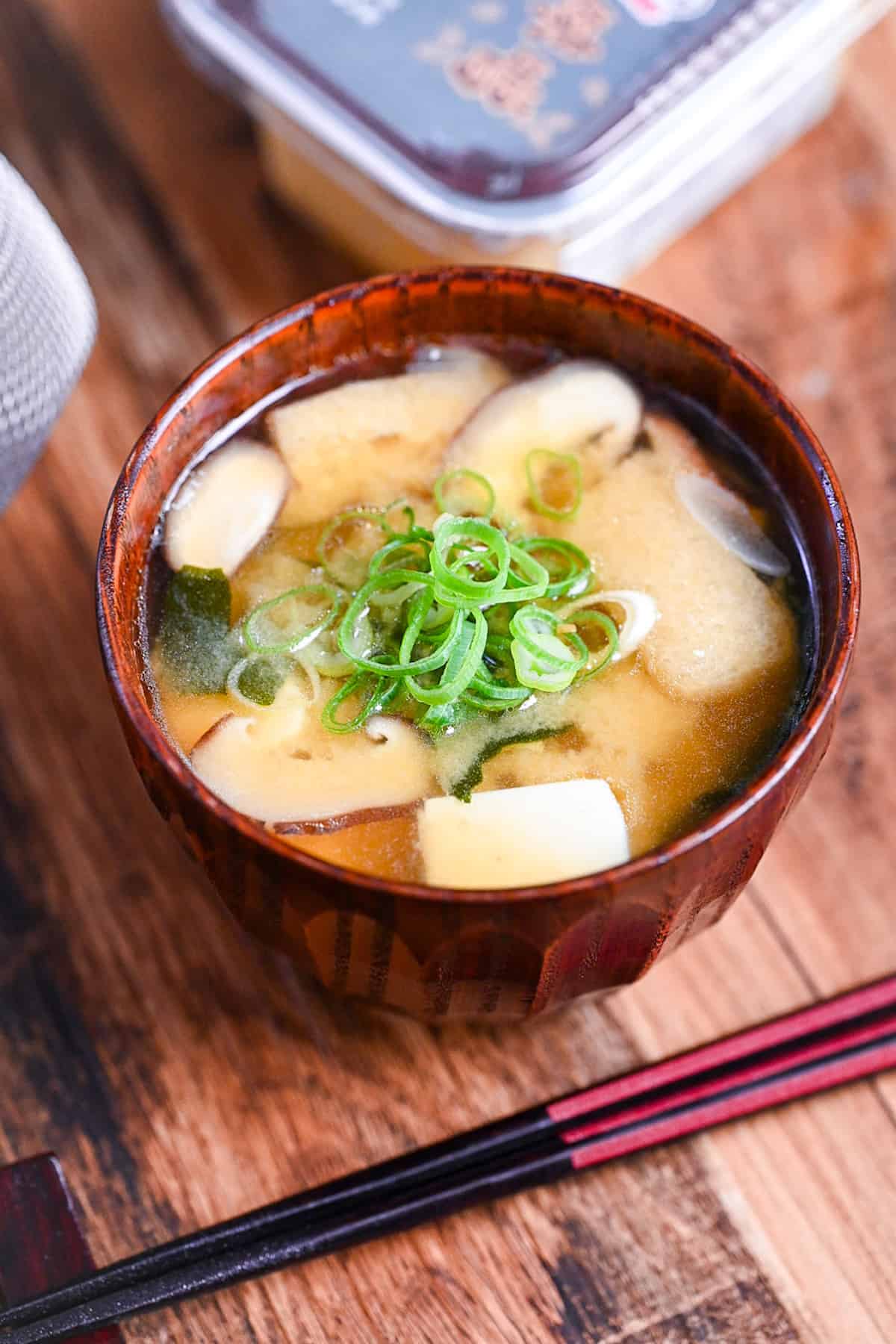 homemade Japanese miso soup in a dark wooden soup bowl with red and black chopsticks