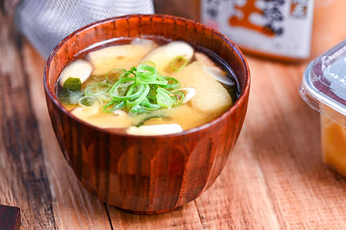 homemade Japanese miso soup in a dark wooden soup bowl with red and black chopsticks