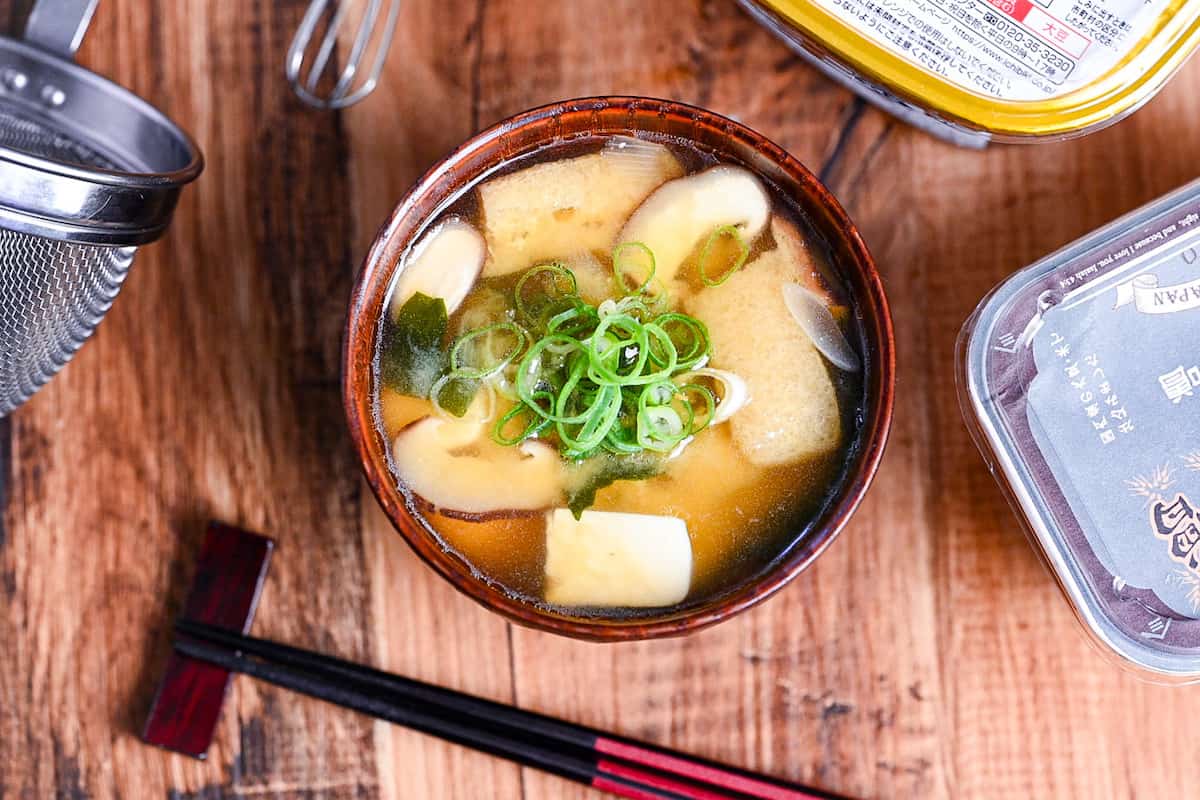 homemade Japanese miso soup in a dark wooden soup bowl with red and black chopsticks