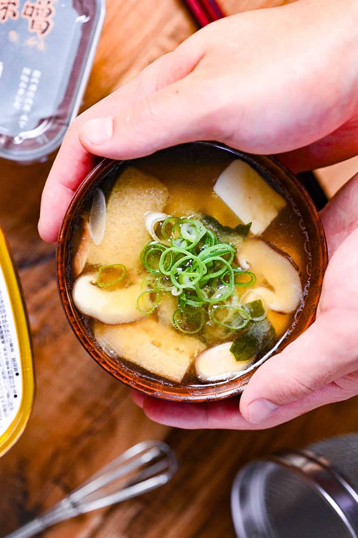 homemade Japanese miso soup in a dark wooden soup bowl with red and black chopsticks