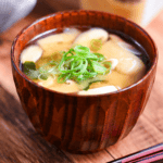 homemade Japanese miso soup in a dark wooden soup bowl with red and black chopsticks