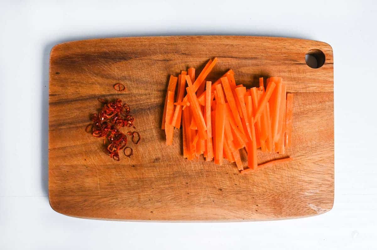 julienned carrot and thinly sliced chili on a wooden chopping board
