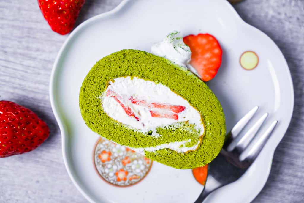 a slice of matcha roll cake with fresh cream and strawberries with dessert fork