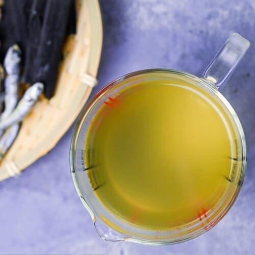 awase dashi made with kombu, bonito and niboshi in a glass measuring jug on a gray background