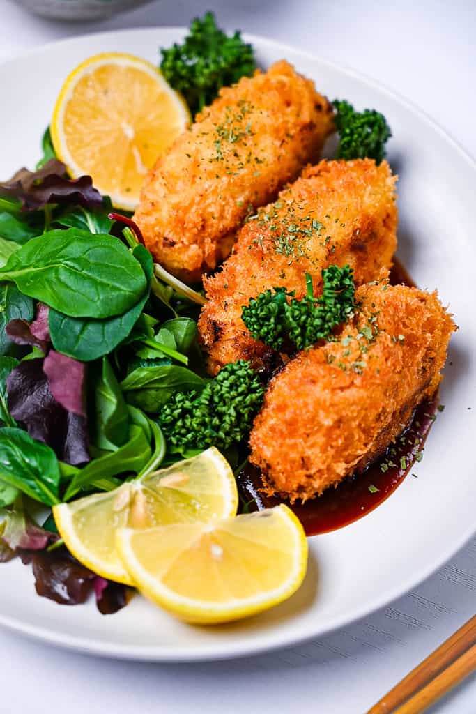 kani cream croquette on a white plate with salad and homemade sauce