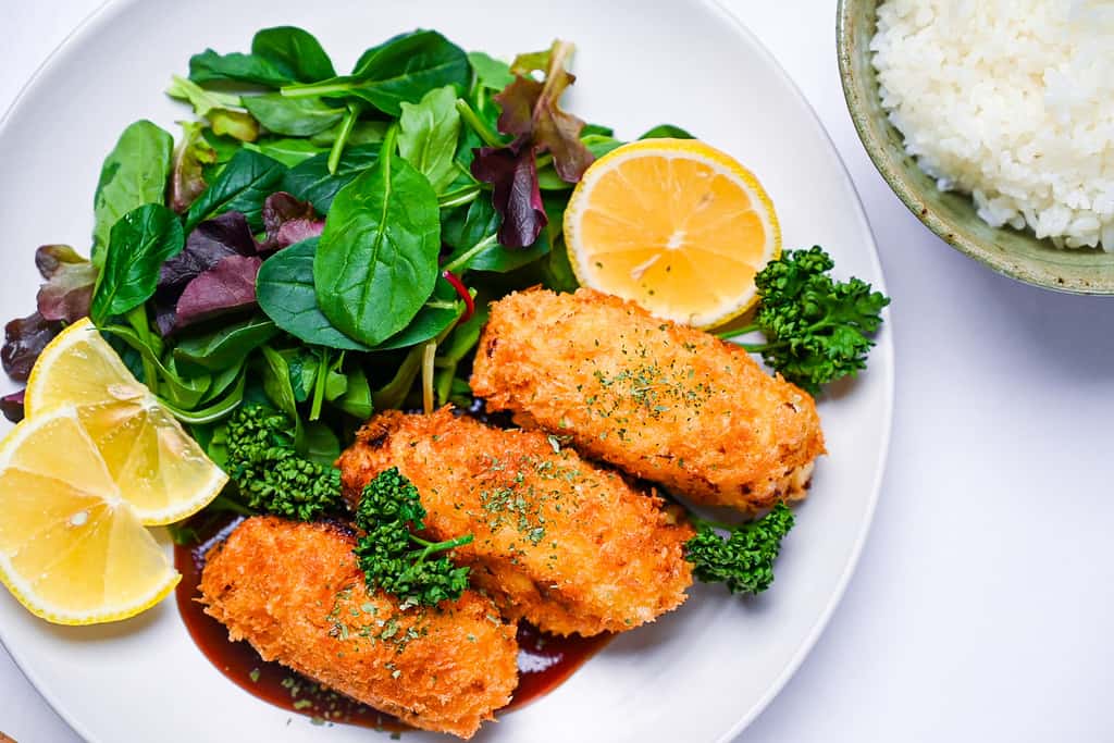 kani cream croquette on a white plate with salad and homemade sauce