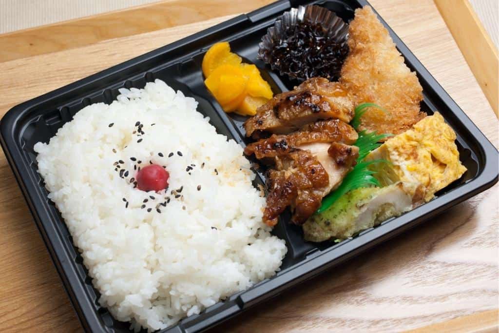 a bento box with rice, chicken, fried fish, hijiki salad, takuan pickles and tamagoyaki