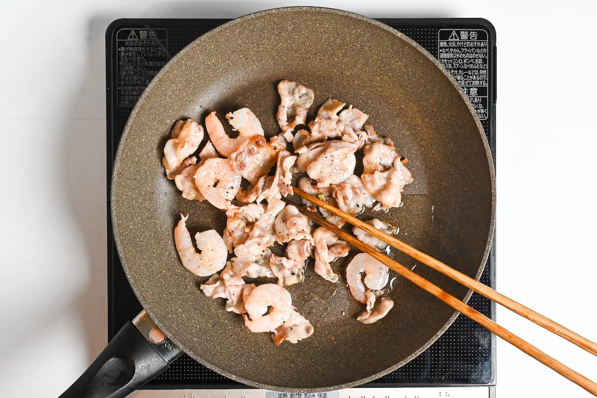 Thinly sliced pork and shrimps frying in a frying pan