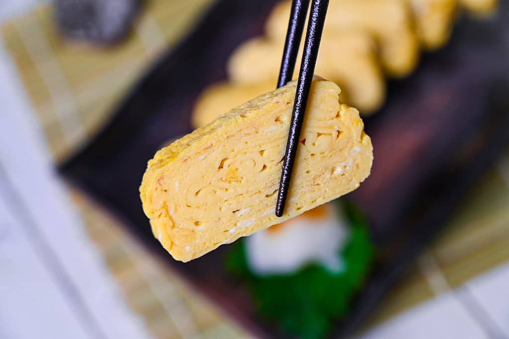 one piece of dashimaki tamago held with black chopsticks