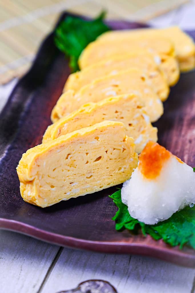 Pieces of sliced dashimaki tamago served on a brown plate with grated daikon