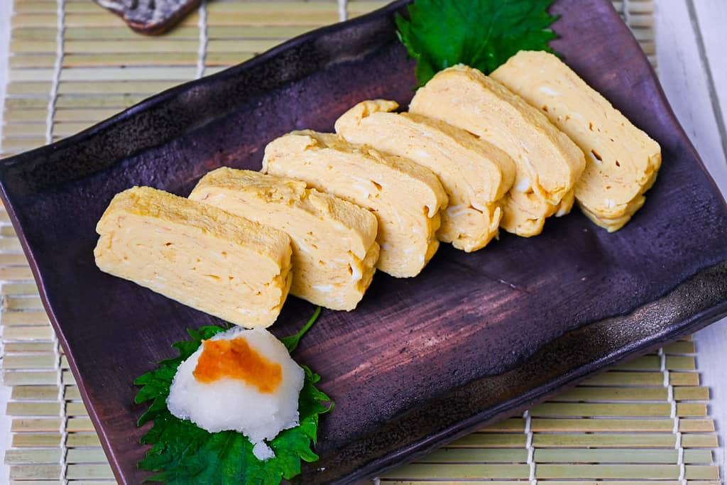 Pieces of sliced dashimaki tamago served on a brown plate with grated daikon