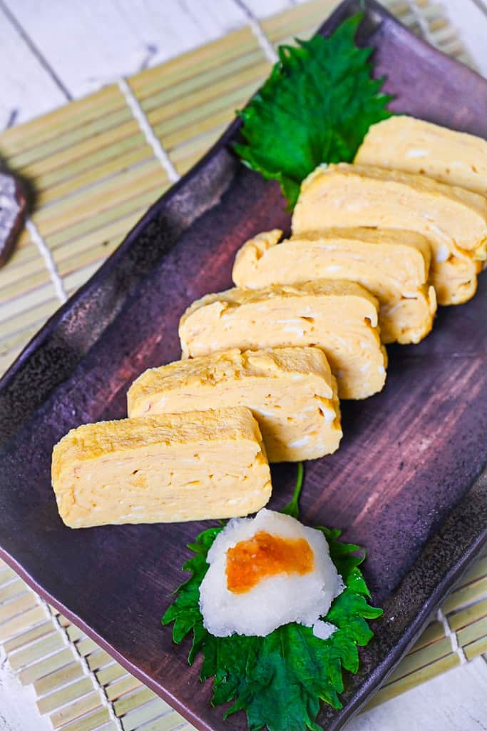 Pieces of sliced dashimaki tamago served on a brown plate with grated daikon