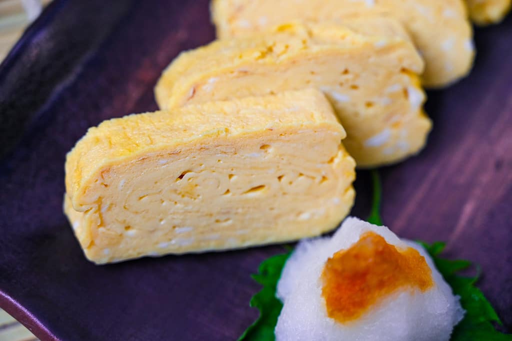 Pieces of sliced dashimaki tamago served on a brown plate with grated daikon