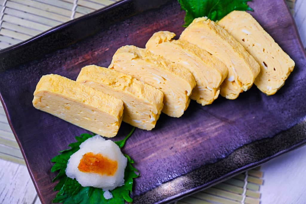 Pieces of sliced dashimaki tamago served on a brown plate with grated daikon