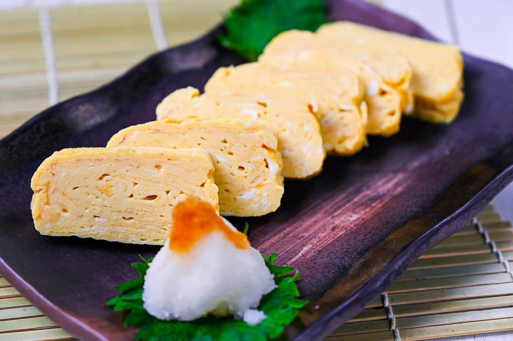 Pieces of sliced dashimaki tamago served on a brown plate with grated daikon