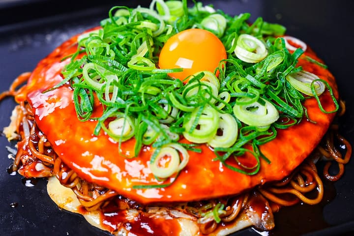 Hiroshima Style Okonomiyaki topped with chopped spring onions and an egg yolk