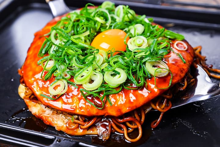 Hiroshima Style Okonomiyaki topped with chopped spring onions and an egg yolk