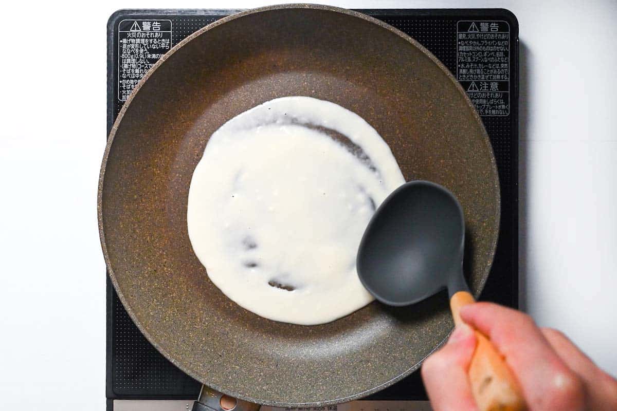 Spreading Hiroshima style okonomiyaki batter in a heated frying pan