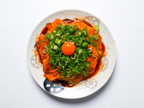 Hiroshima style okonomiyaki topped with sweet sauce, chopped spring onion and an egg yolk