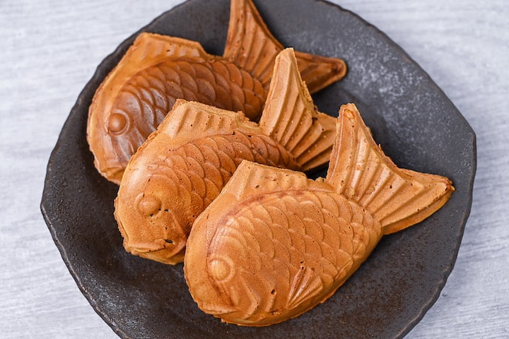 Three golden Taiyaki (fish shaped red bean cake) on a brown plate