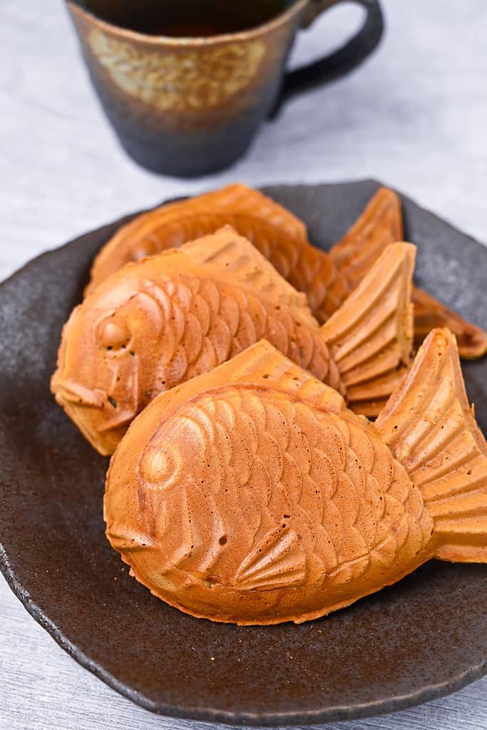 Three golden Taiyaki (fish shaped red bean cake) on a brown plate
