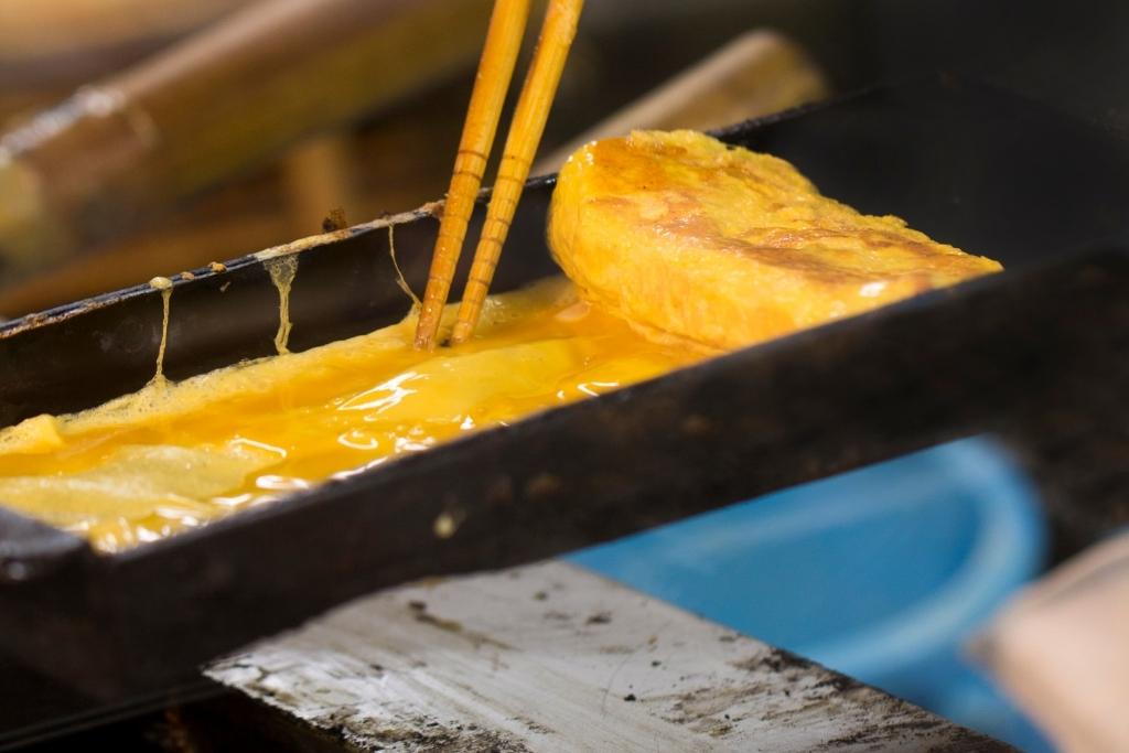 cooking and rolling tamagoyaki in a pan
